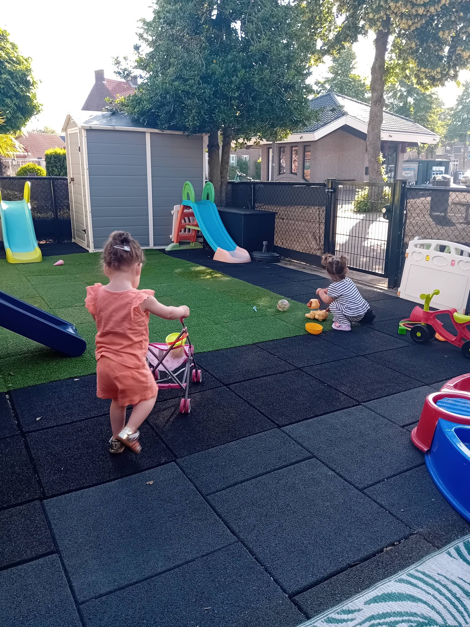 Kinderen spelen in de afgesloten tuin met glijbanen, rubberen valtegels en kunstgras